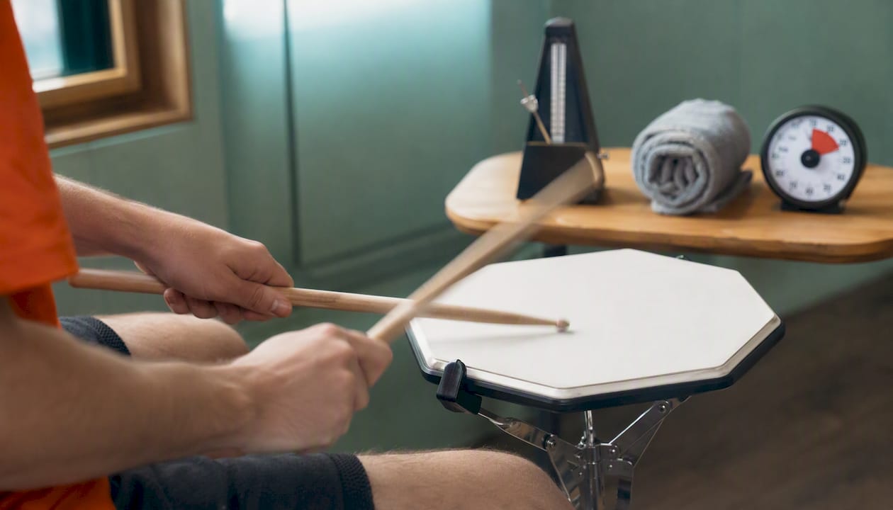 Van bovenaf gefotografeerde handen die enkele slagen oefenen op een oefenpad voor drums